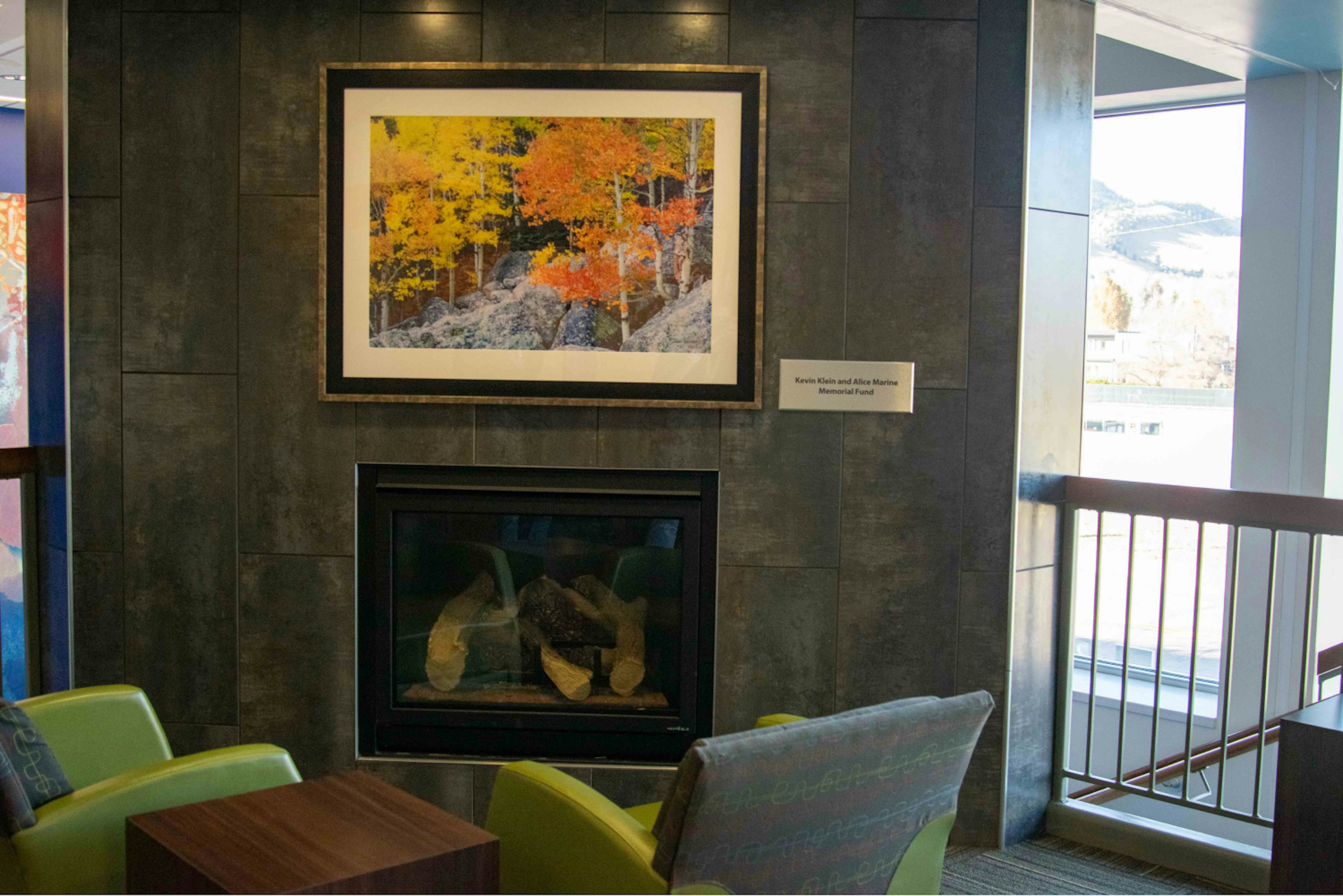 Ryan Wellness Center Upstairs, fireplace with photo of autumn scene. Two green lounge chairs facing fireplace.