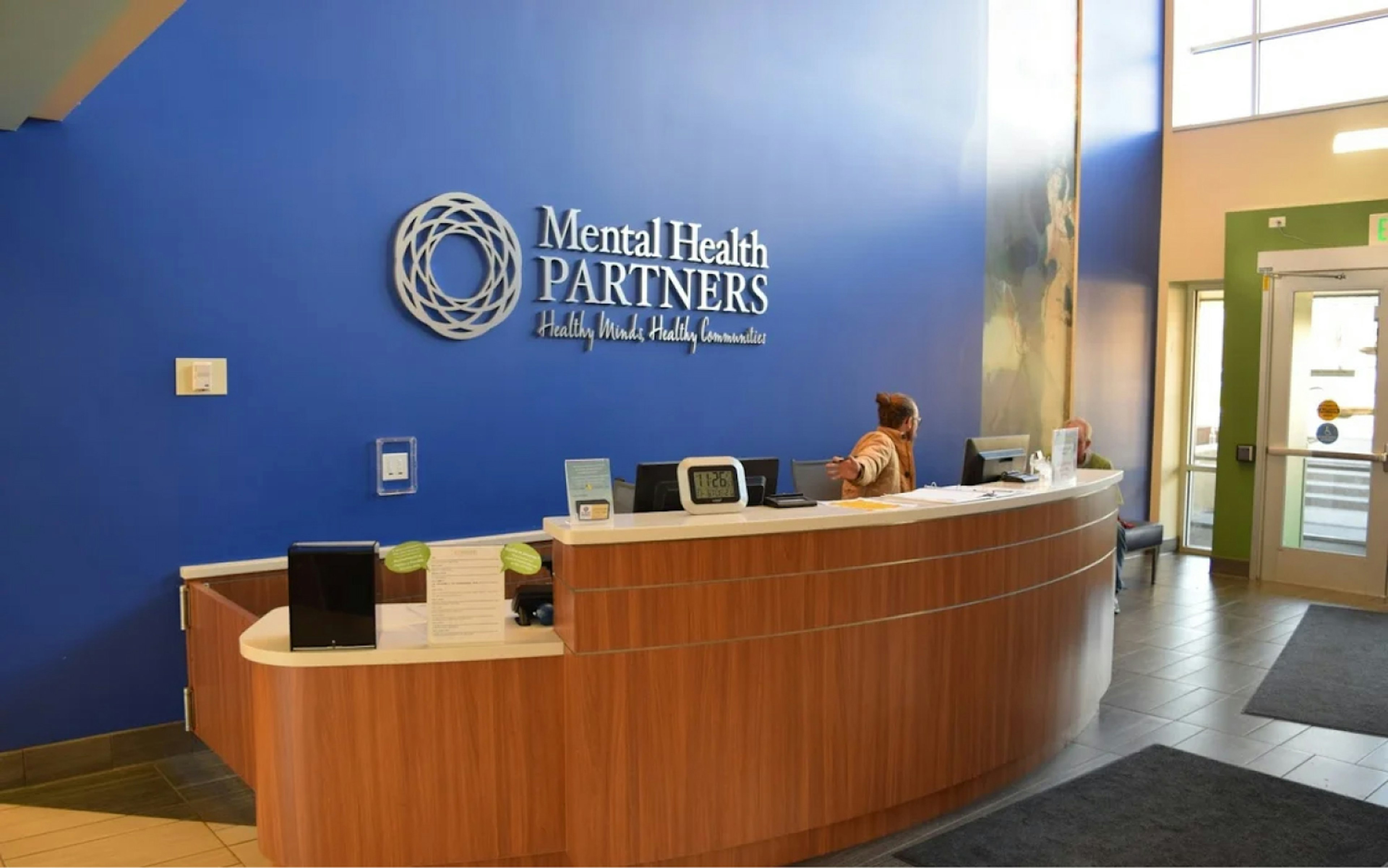Ryan Wellness Center front desk. Featuring blue accent wall with Mental health Partners logo.